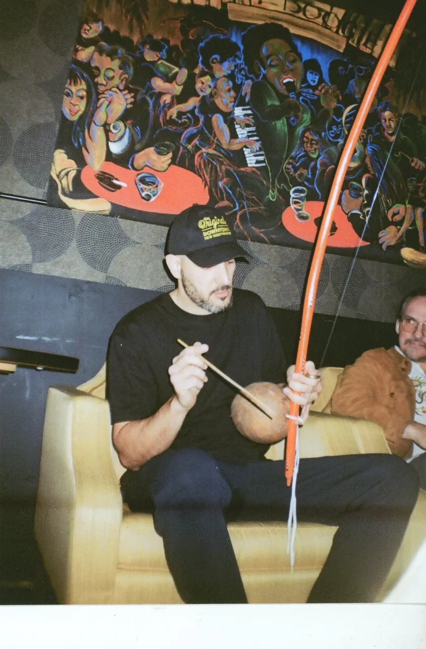 A musician playing berimbau on a couch in front of a painted mural