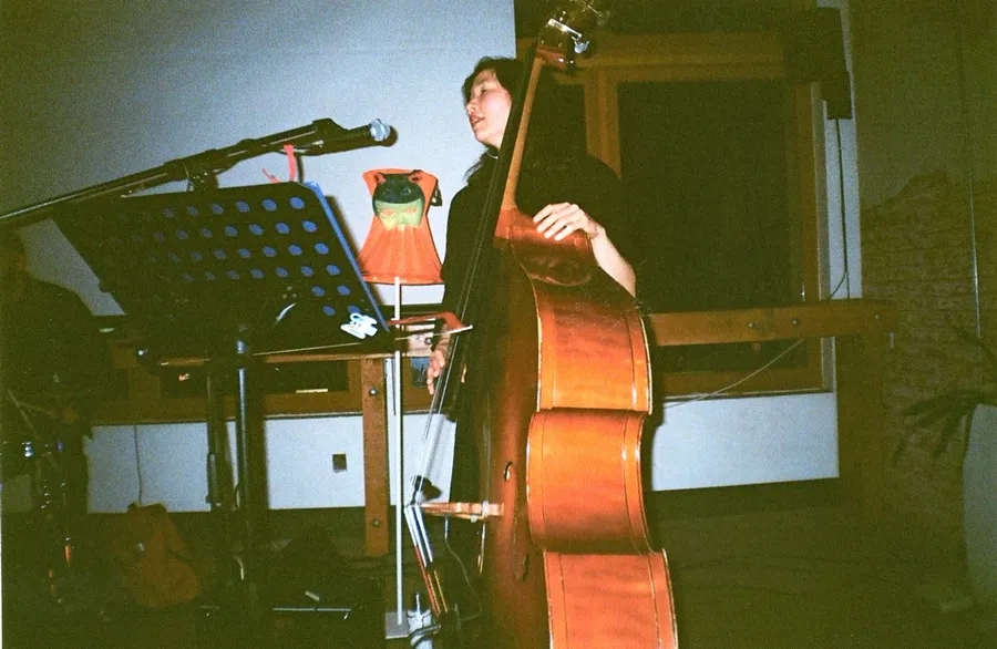 Julia Farry playing upright bass beside a lamp with a painted frog shade