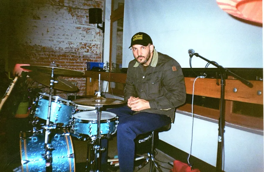 The drummer sitting at his blue kit against a brick wall